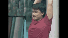 a young man in a red shirt is standing with his arms up in the air .