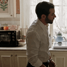a man in a white shirt is standing in a kitchen looking out a window