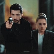 a man is pointing a gun at a woman who is looking at him .