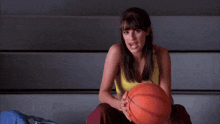 a woman in a yellow tank top sits with a basketball