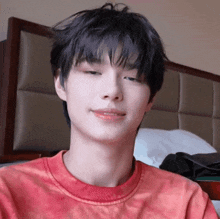 a young man wearing a red tie dye shirt is sitting on a bed