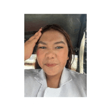 a woman in a white coat is sitting in a car and touching her forehead .
