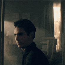 a man in a black shirt is standing in front of a window in a dark room