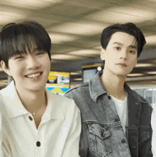 two young men are standing next to each other and smiling . one of the men is wearing a denim jacket .