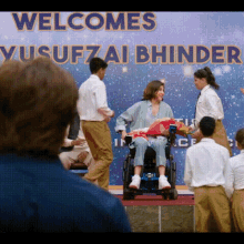 a woman in a wheelchair is standing in front of a banner that says welcomes yusufzai bhinder