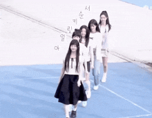 a group of girls are walking in a line on a blue surface with korean writing on it .