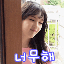 a girl in a pink shirt is peeking out from behind a wooden door with chinese writing on it