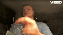 a man wearing headphones is holding a cup with a straw in front of a screen that says " veed "