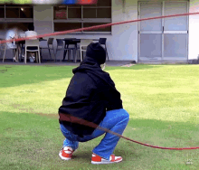 a person squatting down with a red rope in front of a building