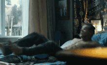 a shirtless man laying on a bed with a boom sign on the wall behind him