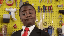 a young boy in a suit and tie is standing in front of a yellow wall with tools on it .