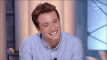 a man in a blue shirt is smiling while sitting at a table with a microphone .