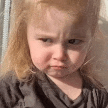 a little girl with blonde hair is making a funny face while wearing a gray shirt ..
