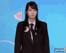 a woman in a suit and tie is standing in front of a blue wall .