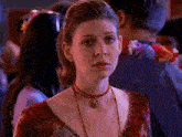 a woman wearing a red necklace with a pendant on it looks at the camera
