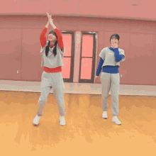 two girls are dancing in a room with a pink wall