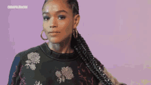 a woman wearing hoop earrings and a braided ponytail stands in front of a cosmopolitan.com logo