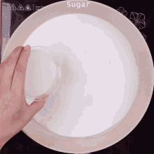 a person pouring sugar into a bowl that says sugar on it