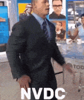 a man in a suit and tie is standing in front of a table that says nvdc on it