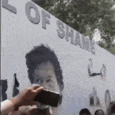 a man is taking a picture of a billboard that says ' l of shame ' on it