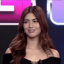a woman in a black off the shoulder top stands in front of a pink and blue background