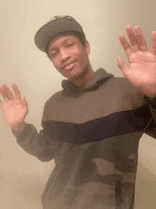 a young man wearing a hat and a camo sweater waves his hands