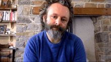 a man with a beard is sitting in front of a stone wall and has the hashtag @itsscottiesstark on the bottom