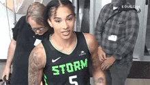 a woman in a black and green basketball jersey is standing in front of a man in a plaid shirt .