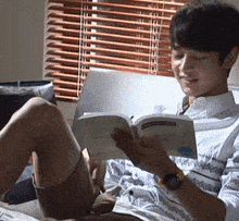 a young man is reading a book in front of a window