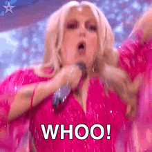 a woman in a pink dress is singing into a microphone and says whoo !