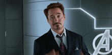 a man in a suit and tie is standing in front of an avengers sign