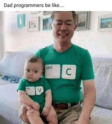 a man is holding a baby wearing a green shirt with ctrl c and v on it