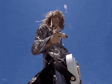a man with long hair is standing in front of a blue sky holding a guitar