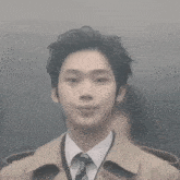 a man in a trench coat and tie is looking at the camera