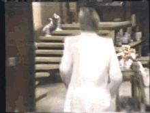 a woman in a white robe is walking down stairs in a room .