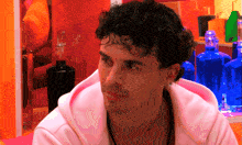 a man with curly hair is wearing a pink sweatshirt