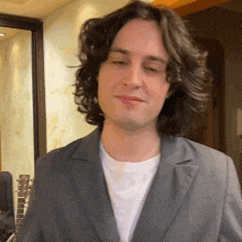 a man with long curly hair wearing a suit and a white shirt