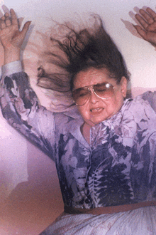 a woman wearing sunglasses and a floral shirt is laying on her back