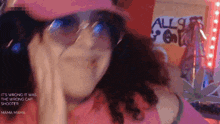 a woman wearing sunglasses and a pink hat is making a funny face in front of a sign that says all