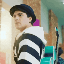 a man wearing a hat and a striped shirt is carrying a guitar on his back