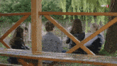 a group of people sitting on a bench with trt 1 written on the fence