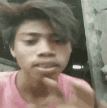 a young man in a pink shirt is making a funny face