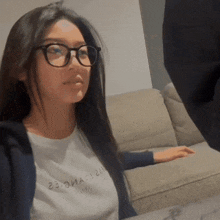 a woman wearing glasses and a t-shirt that says 23 on it sits on a couch