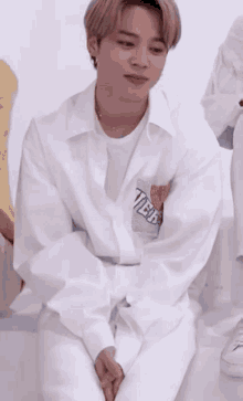 a young man in a white shirt and pants is sitting on a couch with his hands folded .