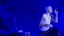 a man in a white tank top is singing into a microphone on stage .