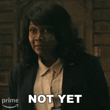 a woman in a suit says " not yet " in front of a bookshelf