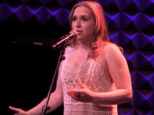 a woman is singing into a microphone in front of a purple wall .