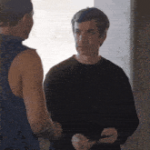 a man in a black sweater is talking to another man in a blue tank top