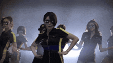 a group of women are dancing in a dark room and one of them is wearing sunglasses and a hat with a star on it