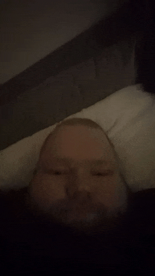 a man with a beard is laying on a bed with his head on a pillow in the dark .